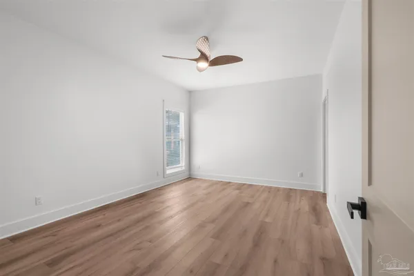 an empty room with wooden floor ceiling fan and windows