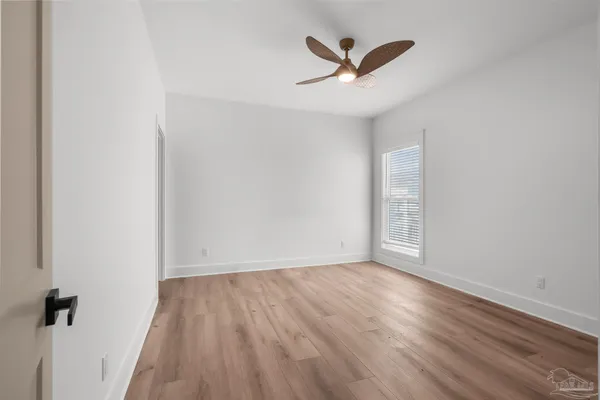 an empty room with wooden floor ceiling fan and windows