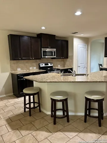 a kitchen with stainless steel appliances granite countertop a table chairs sink and cabinets