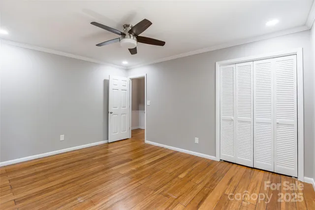 a view of an empty room with wooden floor and a ceiling fan