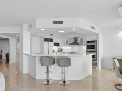 a kitchen with stainless steel appliances granite countertop a kitchen island a stove a sink a refrigerator and chairs