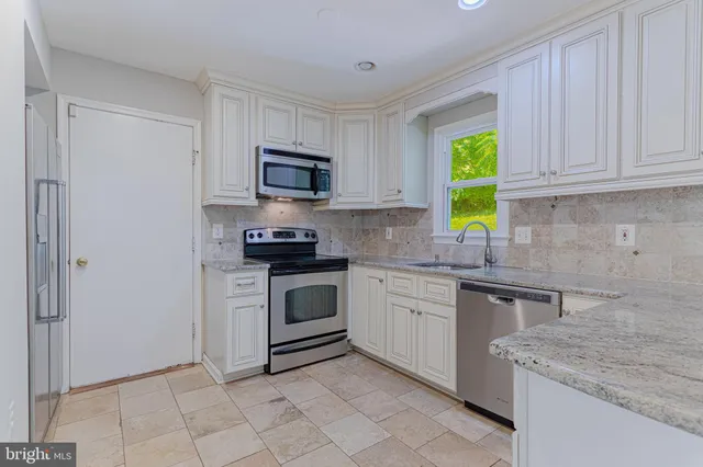 a kitchen with granite countertop a sink a stove top oven and cabinetry