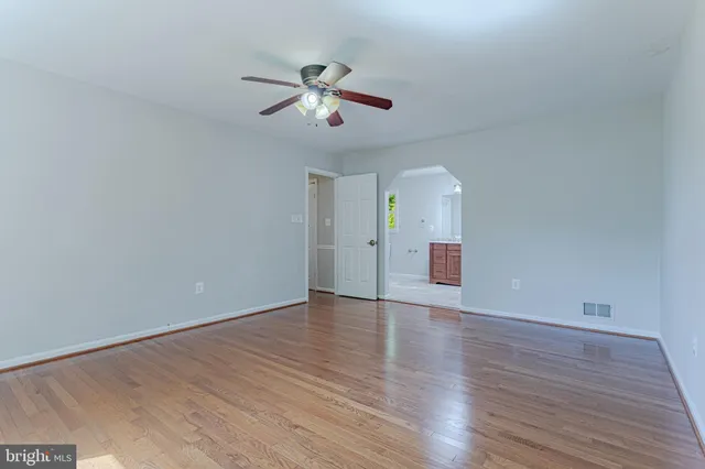 a view of an empty room with wooden floor and a ceiling fan