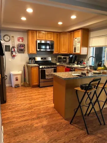 a kitchen with stainless steel appliances granite countertop a stove top oven a sink dishwasher a dining table and chairs with wooden floor