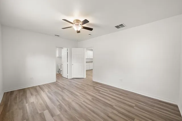 a view of an empty room with wooden floor and a ceiling fan