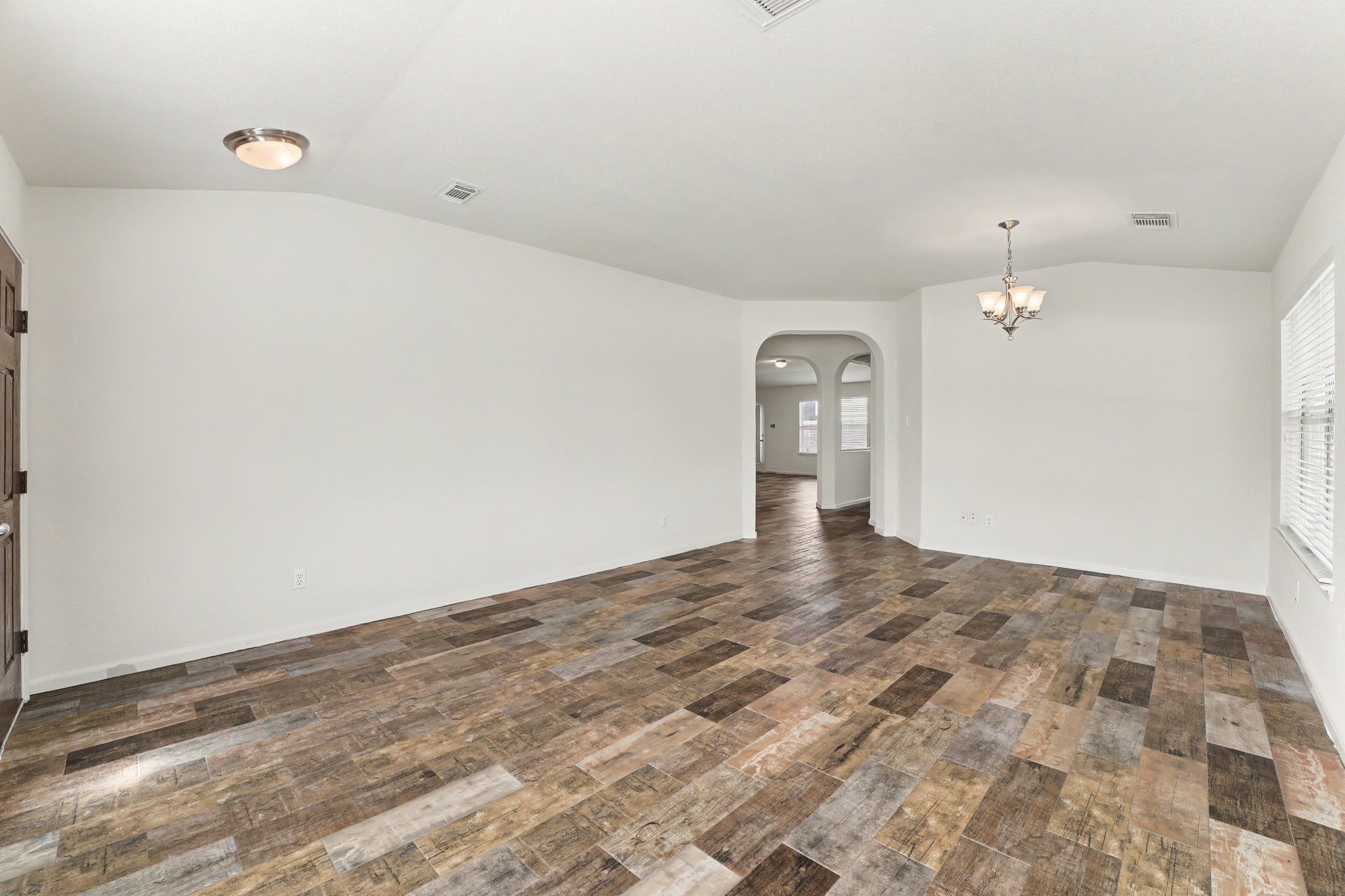 21427 Blooming Rock Lane Spring, TX 77379 - Photo 7 of 32 This spacious room features light walls, dark wood-look flooring, and a stylish chandelier. It has an open layout with arched doorways leading to other areas, creating a warm and inviting atmosphere.