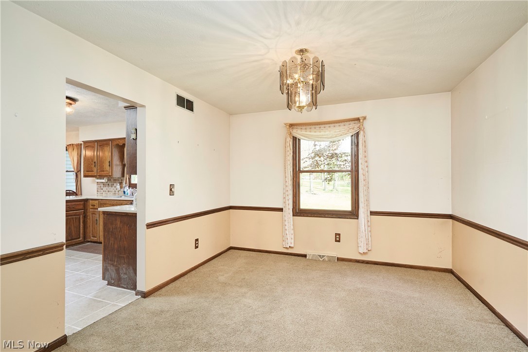 3097 Baughman Road Clinton, OH 44216 - Photo 8 of 27 Carpeted room featuring a decorative chandelier, a window with exterior views, and an arched opening to the kitchen