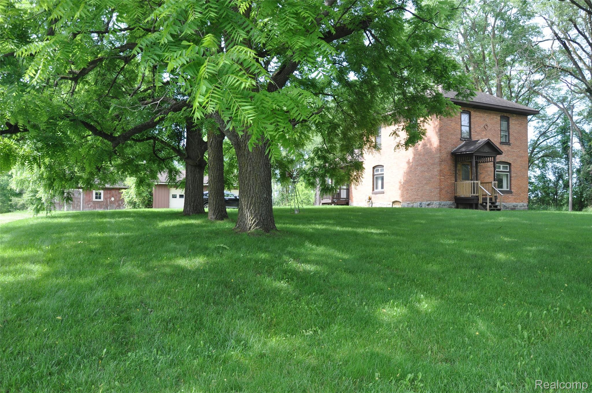 3954 Mayville Road Silverwood, MI 48760 - Photo 3 of 30 Spacious lawn with mature trees, brick exterior, stone foundation, and a covered front porch featuring wooden railing