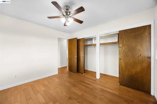 a view of an empty room with wooden floor and a ceiling fan
