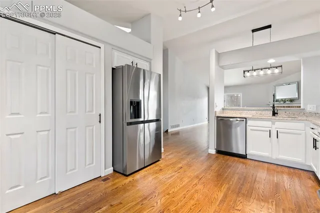 a kitchen with stainless steel appliances granite countertop a refrigerator a sink and white cabinets with wooden floor