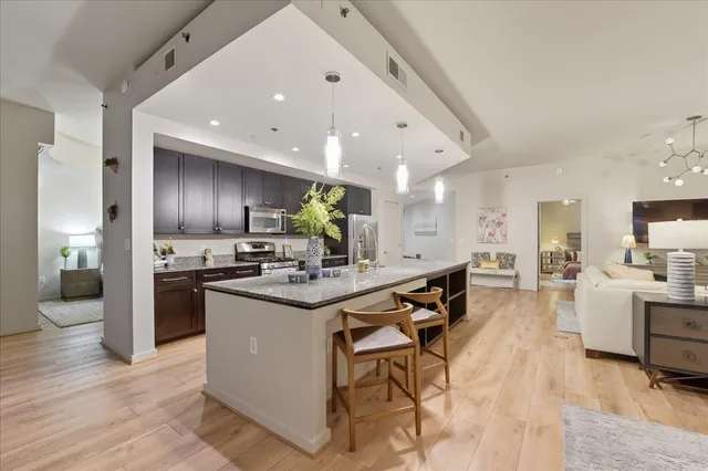 a kitchen with stainless steel appliances kitchen island granite countertop a table chairs stove and cabinets