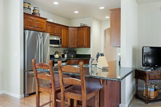 a kitchen with stainless steel appliances granite countertop a stove top oven a refrigerator and a dining table with wooden floor