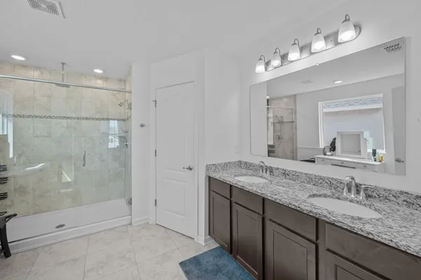 a bathroom with a granite countertop double vanity sink mirror and shower