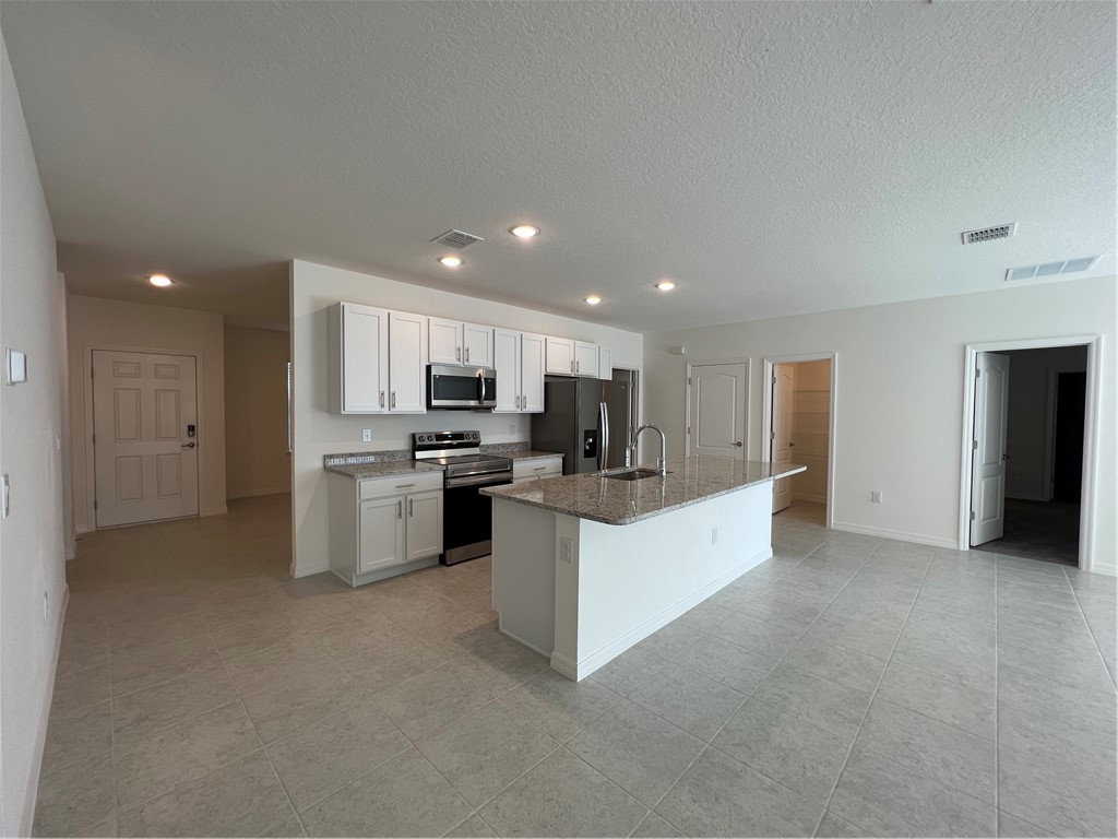 a large white kitchen with stainless steel appliances granite countertop a large counter top and a stove top oven