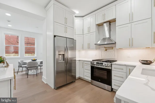 a kitchen with stainless steel appliances a stove a refrigerator and chairs
