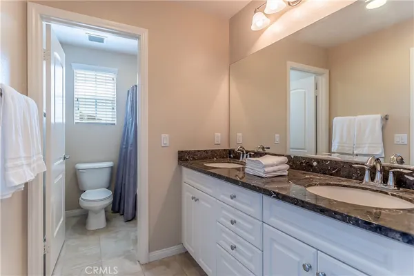a bathroom with a granite countertop double vanity sink a mirror and a toilet