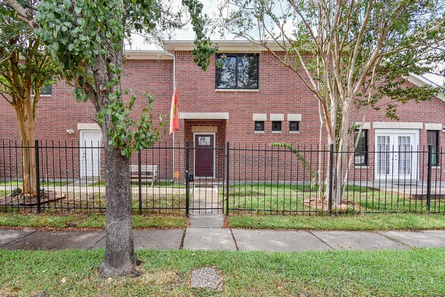 a view of a brick house in front of a yard and plants