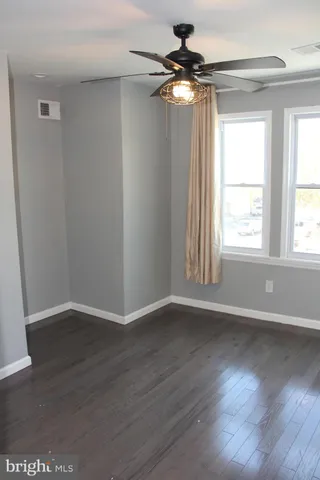 an empty room with wooden floor fan and windows