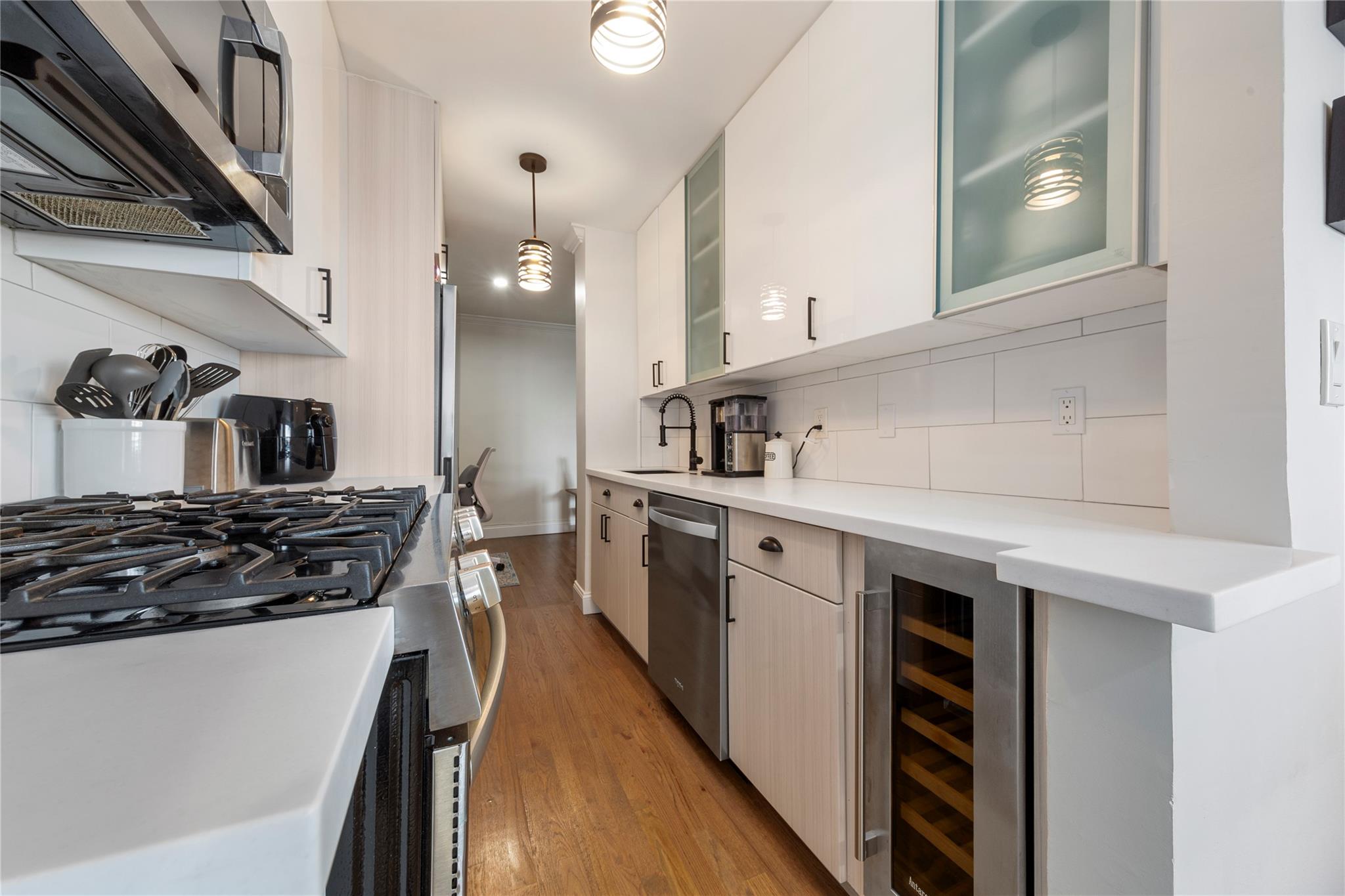 Kitchen featuring stainless steel appliances, beverage cooler, decorative backsplash, light countertops, and light wood flooring