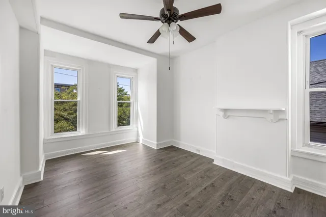 an empty room with wooden floor fan and windows