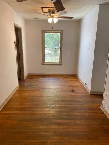 an empty room with wooden floor chandelier fan and windows