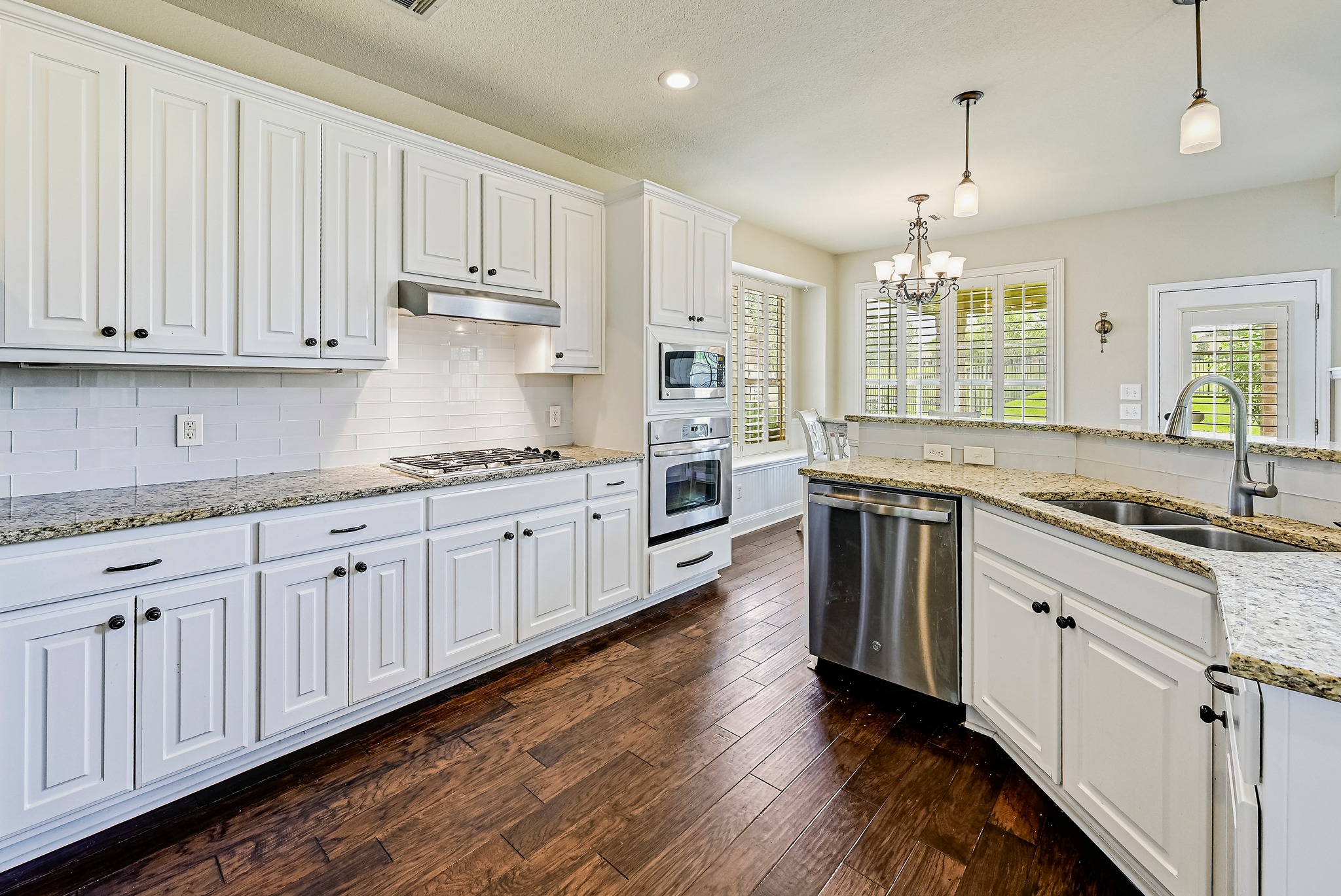 2408 Amen Corner Road Pflugerville, TX 78660 - Photo 16 of 40 Kitchen featuring white cabinetry, granite countertops, stainless steel appliances, wood-finish flooring, and a subway tile backsplash