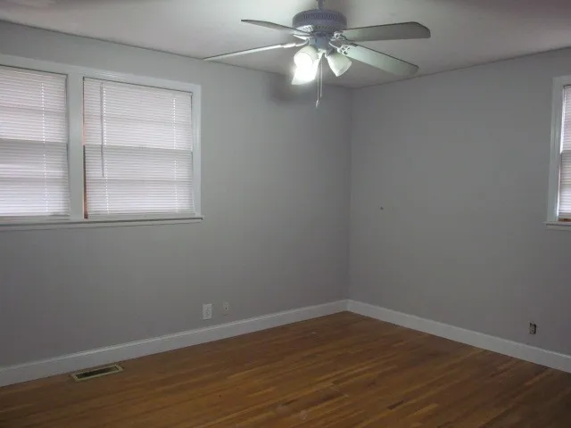 an empty room with wooden floor closet and windows