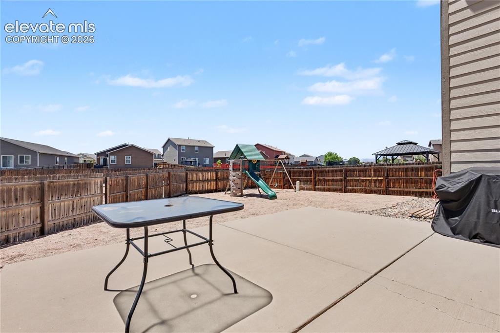 6598 Alliance Loop Colorado Springs, CO 80925 - Photo 36 of 39 Concrete patio area with a wooden privacy fence, gravel landscaping, and a visible play structure