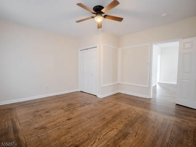 an empty room with wooden floor chandelier fan and windows