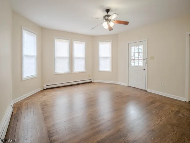an empty room with wooden floor chandelier fan and windows