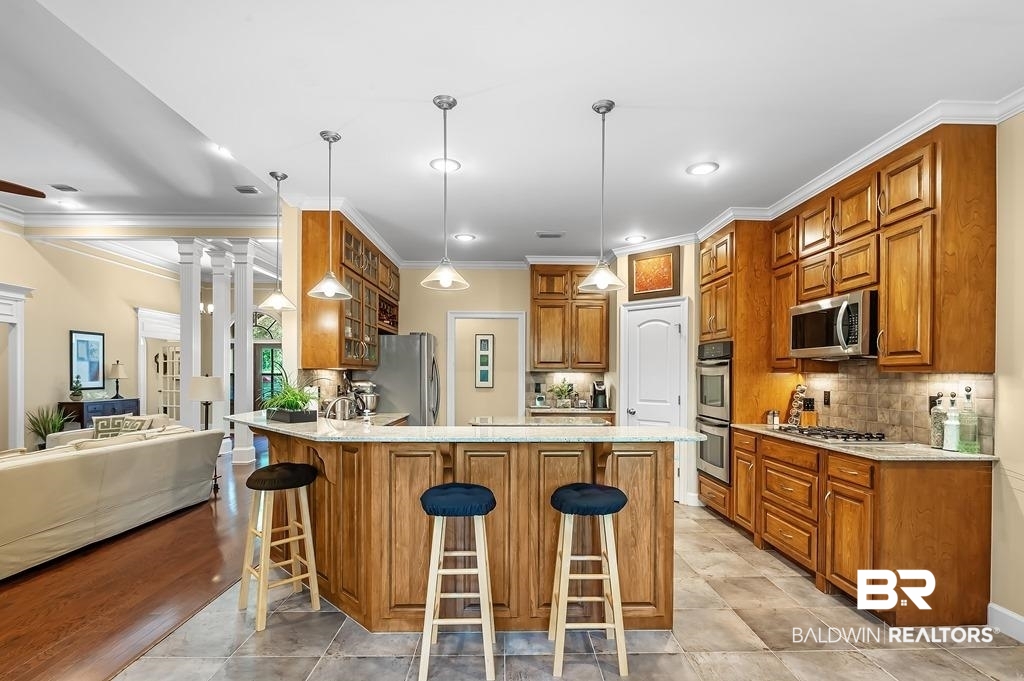 29976 Dolive Ridge Daphne, AL 36527 - Photo 23 of 58 Kitchen featuring appliances with stainless steel finishes, a breakfast bar area, tasteful backsplash, decorative columns, and light tile patterned floors
