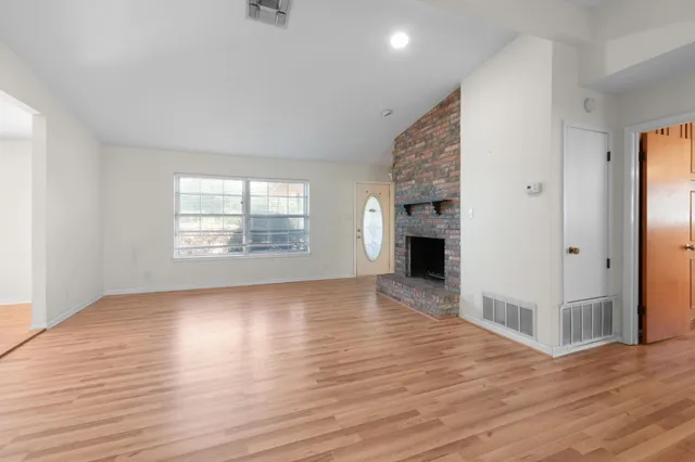 an empty room with wooden floor fireplace and windows