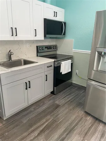 a kitchen with stainless steel appliances white cabinets a sink a stove a microwave and wooden floors