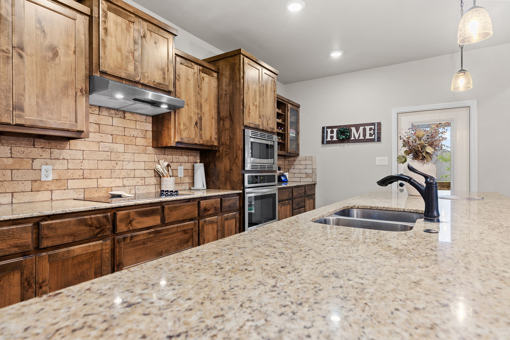 161 Greg Lane Jarrell, TX 76537 - Photo 14 of 35 Kitchen featuring a granite island with dual basin sink and black faucet, wood cabinetry, brick-style backsplash, built-in stainless steel appliances, and recessed lighting