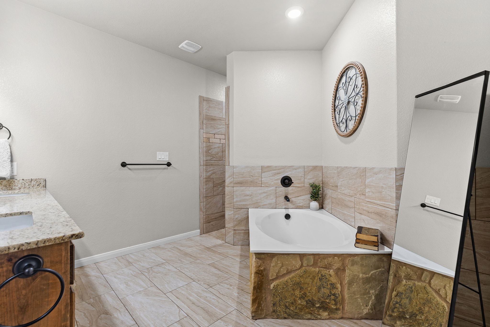 161 Greg Lane Jarrell, TX 76537 - Photo 29 of 35 Bathroom featuring a corner soaking tub with stone surround, a tiled shower enclosure, and a vanity with a light-toned countertop and wood-finish cabinetry