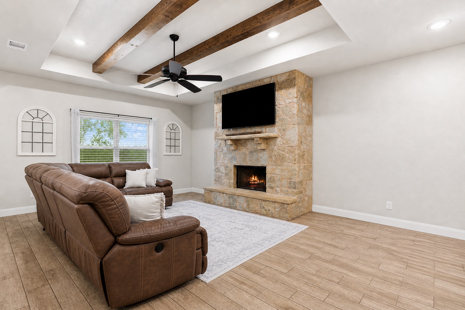 161 Greg Lane Jarrell, TX 76537 - Photo 7 of 35 Living room featuring a stone fireplace with a raised hearth, wood-finish flooring, and a tray ceiling with exposed wood beams