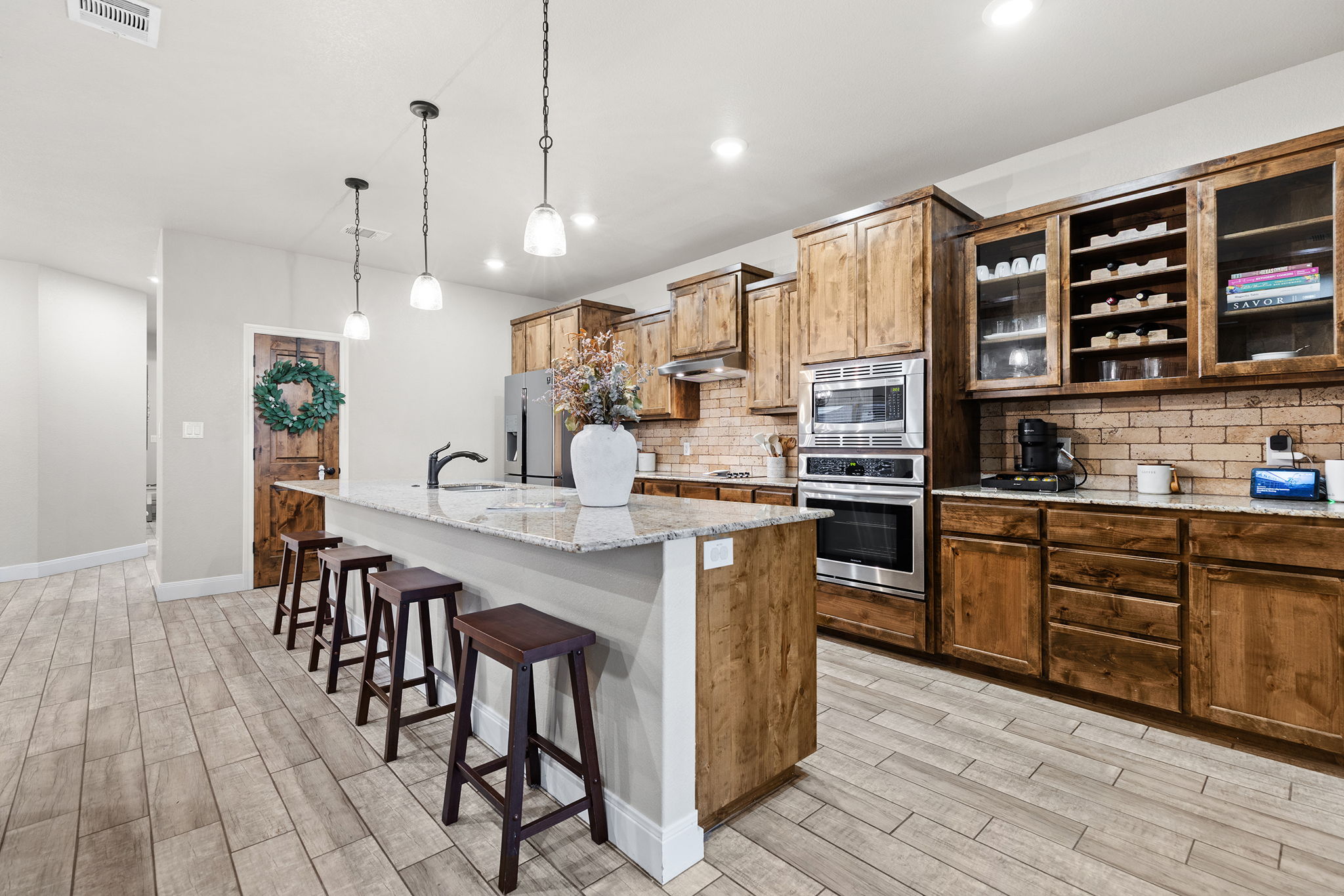 161 Greg Lane Jarrell, TX 76537 - Photo 10 of 35 Kitchen featuring wood-finish flooring, a central island with a light-toned countertop, pendant lighting, built-in stainless steel appliances, and wood cabinetry with glass-front accents