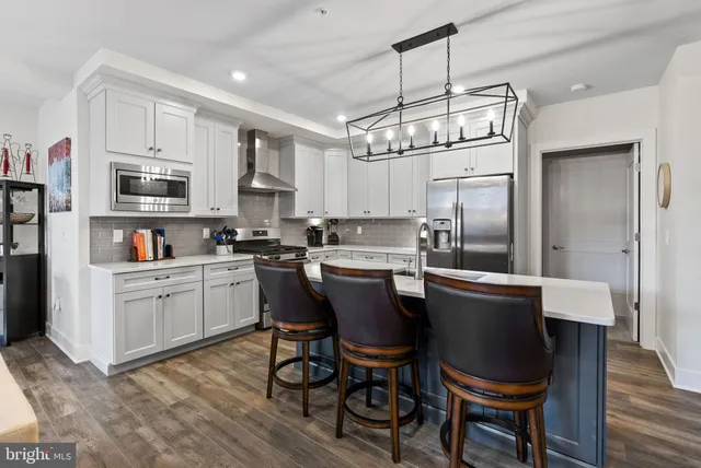 a kitchen with stainless steel appliances granite countertop a sink dishwasher a stove a refrigerator a dining table and chairs with wooden floor