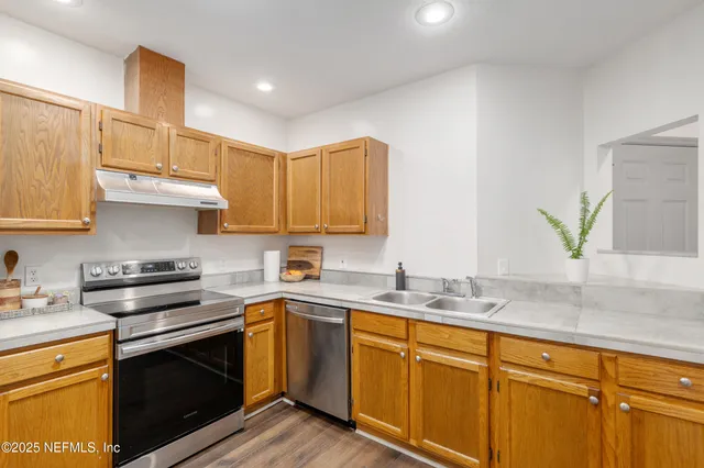 a kitchen with stainless steel appliances granite countertop wooden cabinets a sink and dishwasher a stove with wooden floor