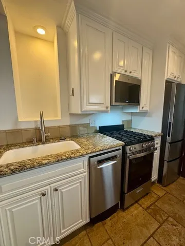 a kitchen with granite countertop a sink stainless steel appliances and white cabinets