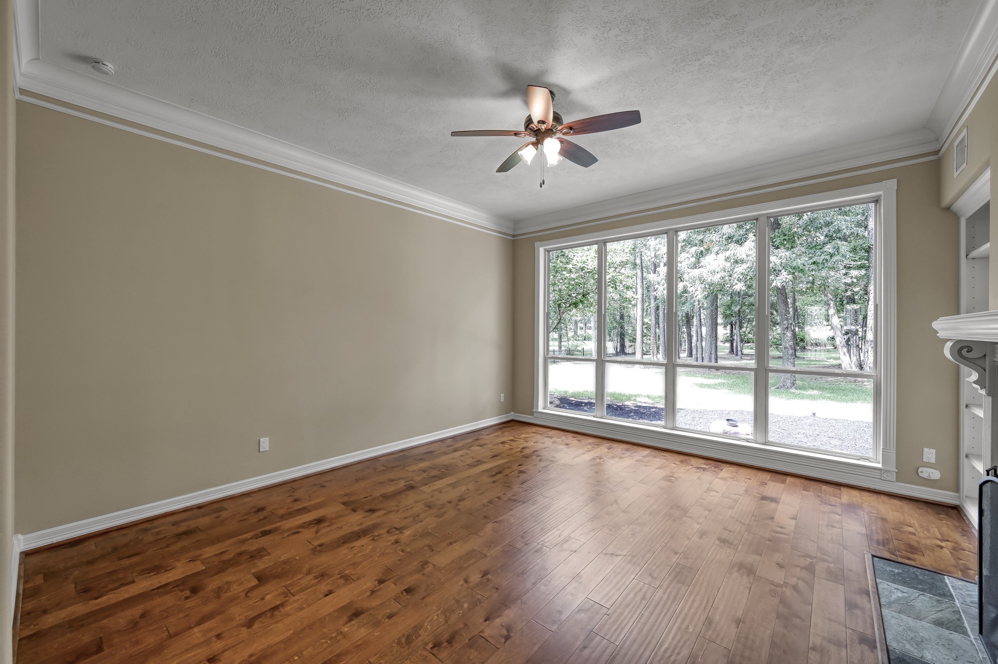 2205 Longmire Road Conroe, TX 77304 - Photo 8 of 49 Enjoy the wall of large windows in the formal living room offering a scenic view of the backyard trees. Features hardwood floors, neutral walls, a ceiling fan, and crown molding for a polished look.