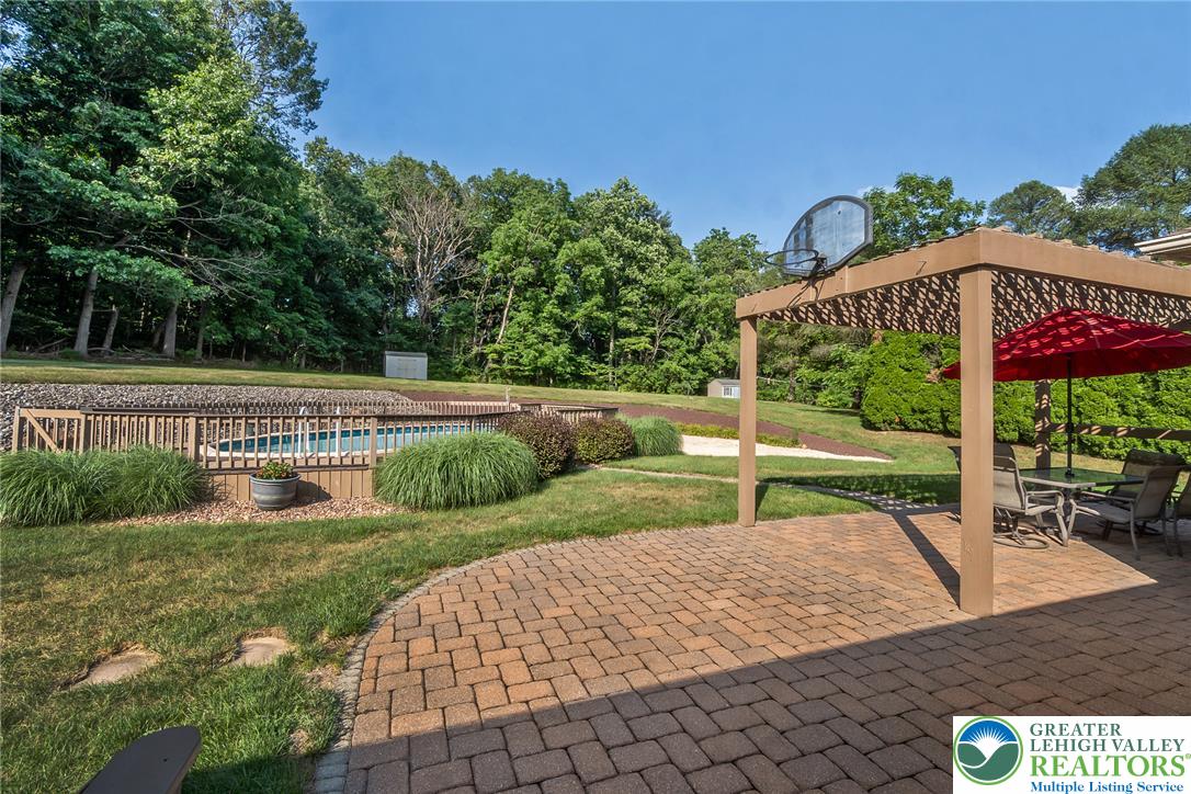 An inviting backyard oasis offers a sparkling pool and a paver patio with a pergola for shaded outdoor dining.