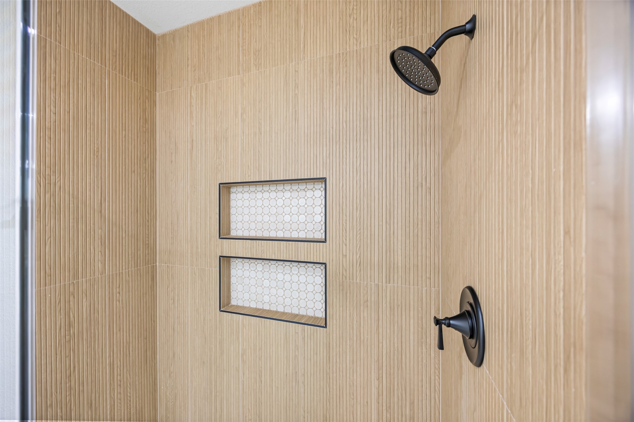 1807 Waco Street Dayton, TX 77535 - Photo 17 of 26 Spacious tiled shower featuring floor-to-ceiling vertical tile, dual built-in niches with mosaic accents, and matte black fixtures.