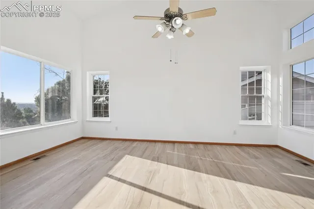 an empty room with wooden floor fan and windows