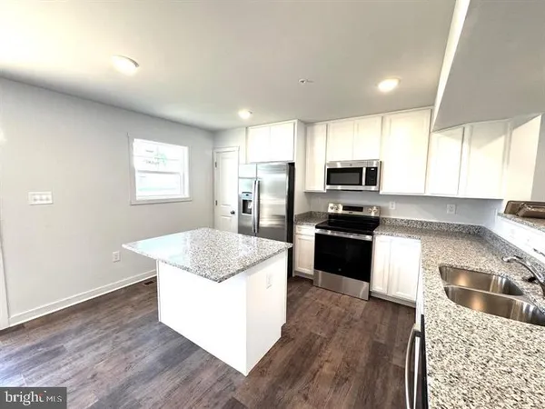 a kitchen with granite countertop a stove top oven a sink dishwasher a refrigerator and white cabinets with wooden floor