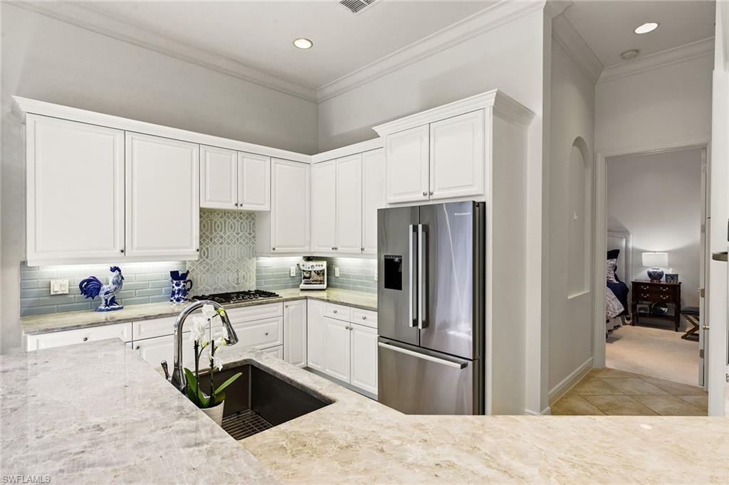 28540 Calabria Court, Unit 102 Naples, FL 34110 - Photo 4 of 32 a kitchen with granite countertop a sink stainless steel appliances and white cabinets