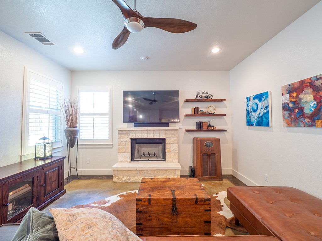 55 Tournament Way, Unit B The Hills, TX 78738 - Photo 12 of 23 Living area featuring a stone fireplace, ceiling fan, finished concrete flooring, recessed lighting, and a textured ceiling