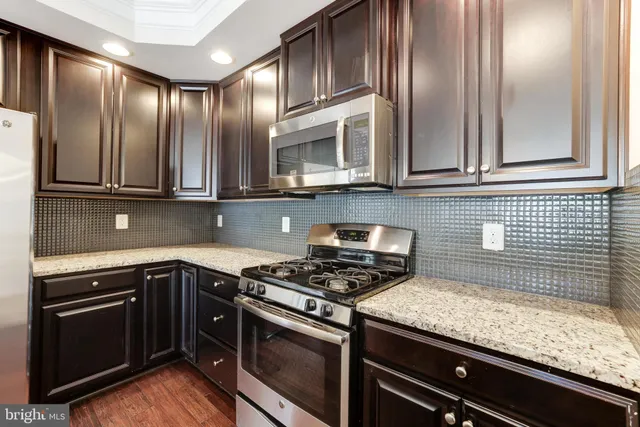 a kitchen with granite countertop stainless steel appliances wooden cabinets a stove and a sink