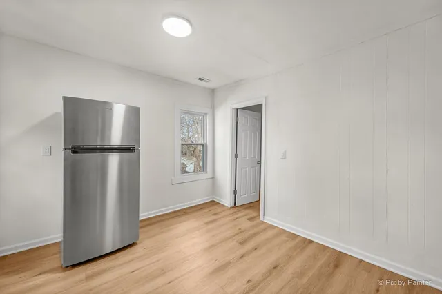a view of empty room with wooden floor and refrigerator