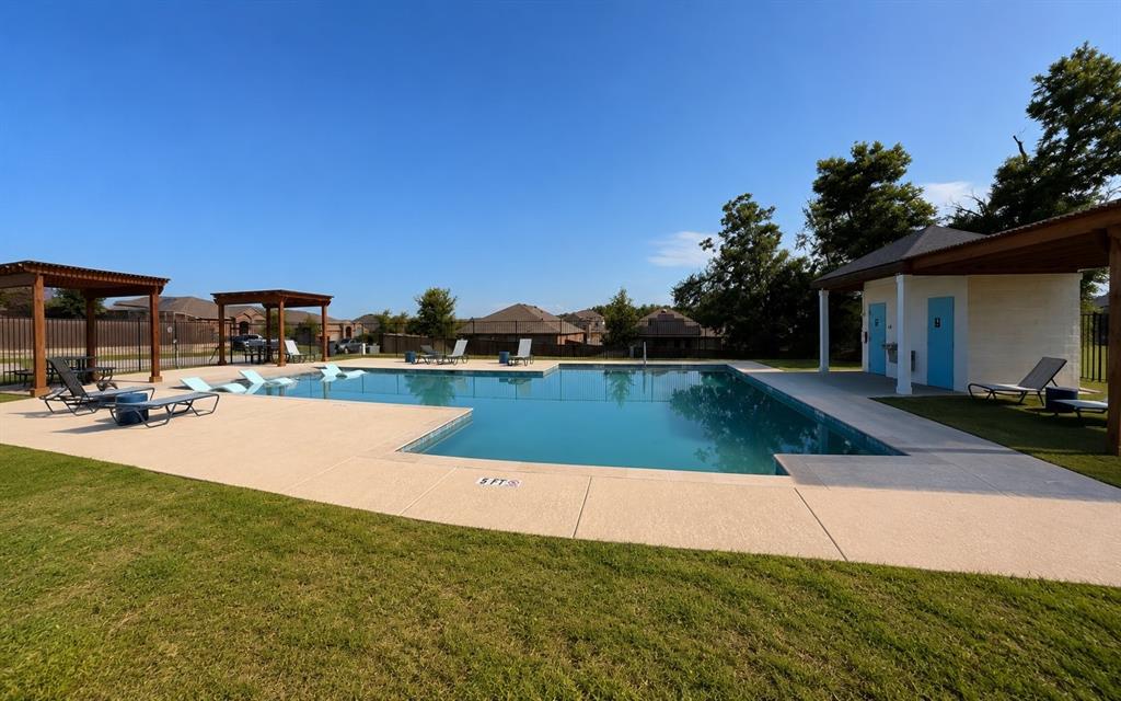 824 Juniper Street Anna, TX 75409 - Photo 25 of 25 Outdoor swimming pool featuring a perimeter fence, surrounding concrete decking, and an adjacent building with blue doors